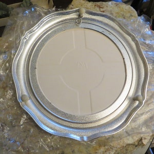 Puede incluir: Un soporte para tartas de metal plateado con un inserto de cer&aacute;mica blanca. El soporte tiene un borde festoneado y tres peque&ntilde;os pies.