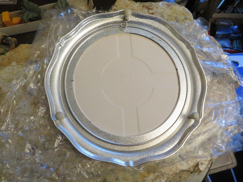 Puede incluir: Un soporte para tartas de metal plateado con un inserto de cer&aacute;mica blanca. El soporte tiene un borde festoneado y tres peque&ntilde;os pies.