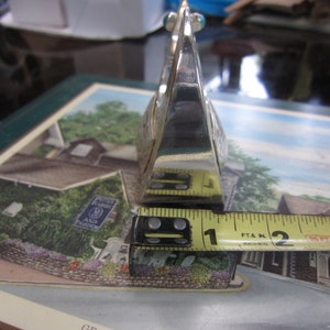 May include: A silver-colored, geometric object with a triangular shape, approximately 2 inches long. The object has a reflective surface and appears to be made of metal. It is positioned on a colorful surface with a printed image.