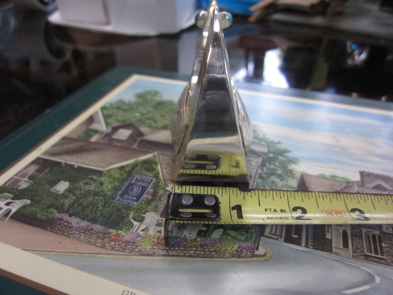 May include: A silver-colored, geometric object with a triangular shape, approximately 2 inches long. The object has a reflective surface and appears to be made of metal. It is positioned on a colorful surface with a printed image.