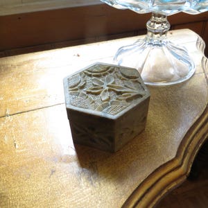 May include: A hexagonal, carved wooden box with a floral design. The box is made of light brown wood and has a natural finish.