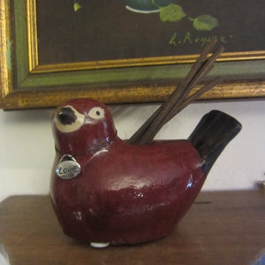 May include: A red ceramic bird figurine with a black tail and a silver charm that says "Love".