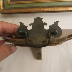 May include: A decorative metal shelf bracket with a ornate, black metal handle. The bracket is attached to a wooden shelf.