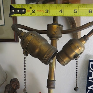 May include: A brass lamp with two sockets and pull chains. The lamp is about 2 feet tall and has a simple design.