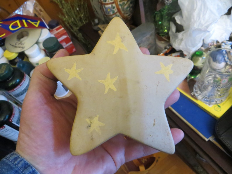 May include: A beige ceramic star with five points, decorated with five yellow stars. The star is slightly textured and has a worn look.