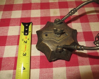 May include: Antique brass oil lamp with a decorative design. The lamp has a chain and a handle. The lamp is on a red and white checkered tablecloth.