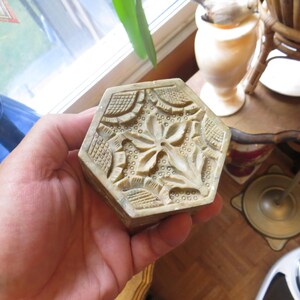 May include: A hexagonal, carved stone box with a floral design. The box is made of a light green stone with intricate details.