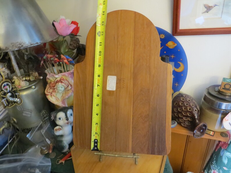 May include: A wooden cutting board with a rounded top and a brass stand. The board is 15 inches tall and has a label that reads "Danish".