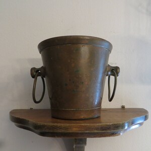 May include: A copper ice bucket with two handles. The bucket is sitting on a wooden shelf.