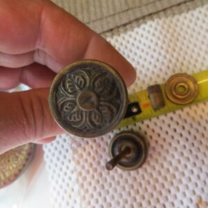 May include: A close-up of a brass knob with a floral design. The knob is being held by a hand.