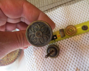 May include: A close-up of a brass knob with a floral design. The knob is being held by a hand.