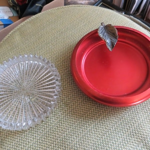 May include: Two decorative dishes, one clear glass with a radial pattern and one red metal with a leaf design.