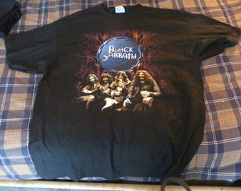 May include: Black Sabbath band t-shirt with a black background and a graphic of the band members in front of a dark forest. The band's name is written in white on a silver drum.