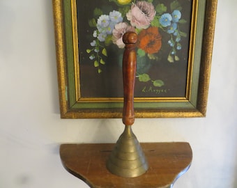 May include: A brass bell with a wooden handle. The bell has a flared, conical shape with multiple ridges. The handle is a dark brown wood with a rounded knob at the top.