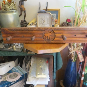 May include: A wooden wall mounted coat rack with four hooks and a carved moose design. The rack is stained a dark brown color.