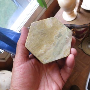 May include: A hand holding a hexagonal shaped, light green and brown stone coaster.
