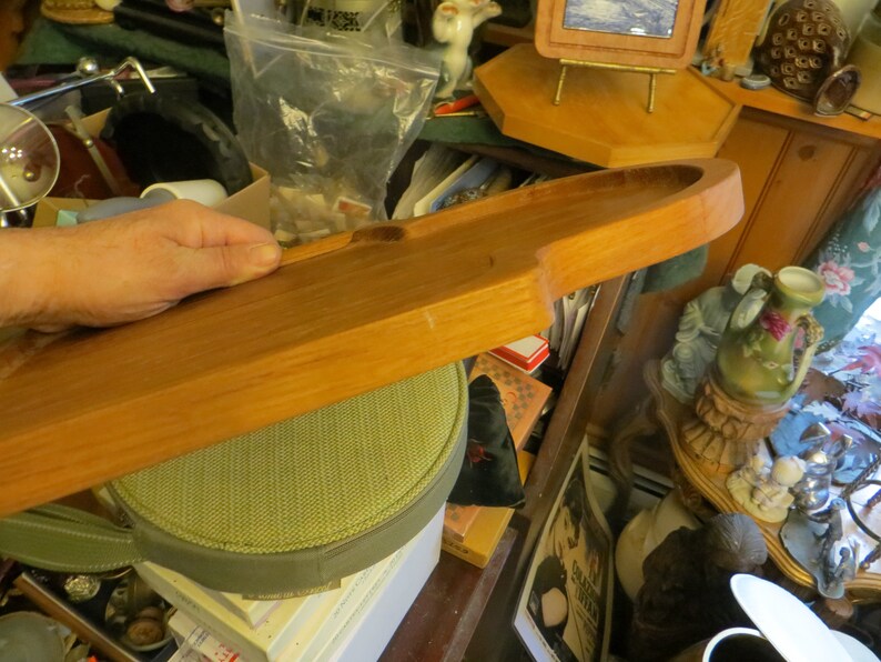 May include: A long, wooden serving tray with a rounded edge. The tray is made of light brown wood and has a smooth, polished finish.