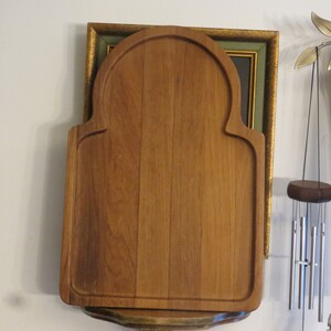 May include: A wooden cutting board with an arched top and a decorative edge. The board is made of light brown wood and has a natural finish.