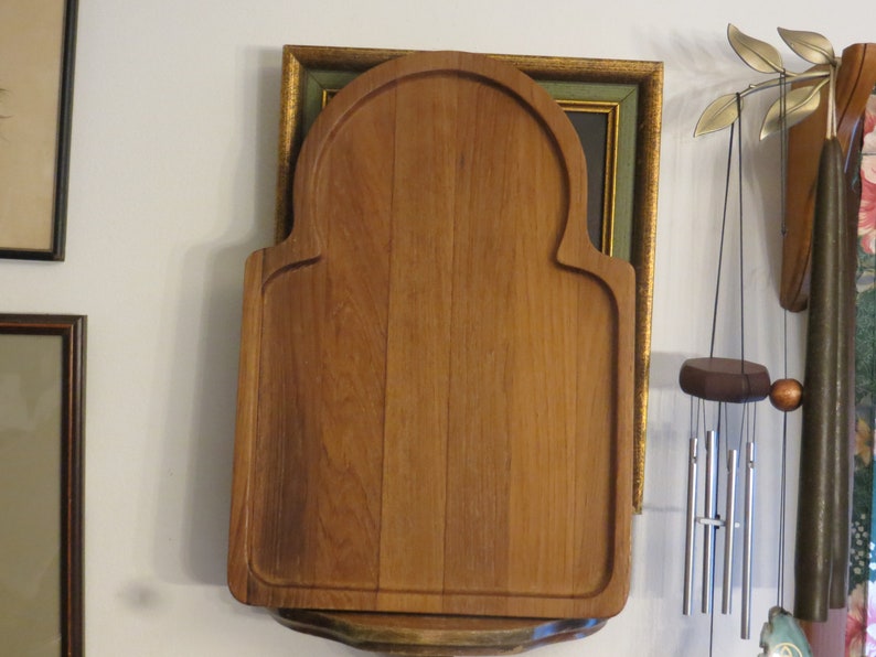 May include: A wooden cutting board with an arched top and a decorative edge. The board is made of light brown wood and has a natural finish.