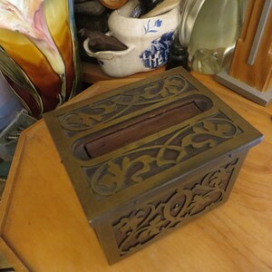 May include: A decorative brass box with an intricate floral design. The box has a wooden lid and is open, revealing the interior.
