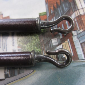 May include: Two brown wooden curtain rods with metal hooks on the ends. The hooks are shaped like a letter S.