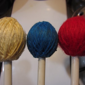 May include: Three yarn-covered mallets with wooden handles. The mallets are yellow, blue, and red.