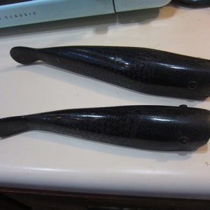May include: Two black plastic fish-shaped objects with a textured surface. The objects are about 10 inches long.