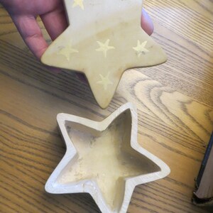 May include: A beige ceramic star-shaped trinket box with gold stars painted on the top. The box is open and the inside is empty.