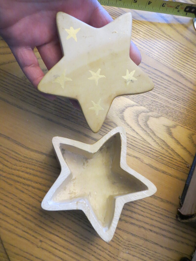 May include: A beige ceramic star-shaped trinket box with gold stars painted on the top. The box is open and the inside is empty.