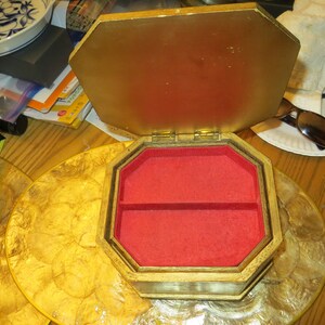 May include: A gold octagonal wooden jewellery box with a red velvet interior. The box has a hinged lid and two compartments.