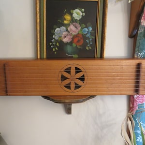 May include: A wooden musical instrument with strings and a carved flower design. The instrument is mounted on a wall shelf.