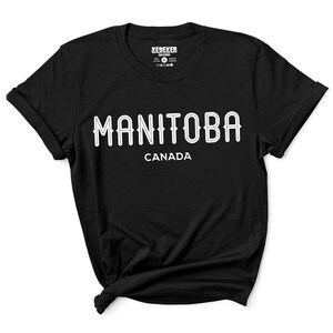 May include: Black t-shirt with the word "MANITOBA" in white, arched text, and "CANADA" below it. The shirt has rolled-up sleeves and a crew neck. The brand name "KEBEKER" is visible on the upper left of the shirt.