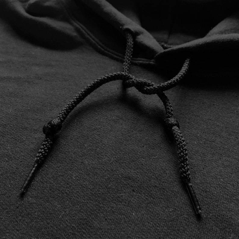 May include: Close-up of a black hoodie with black drawstring ties. The hoodie is made of a soft, textured fabric.