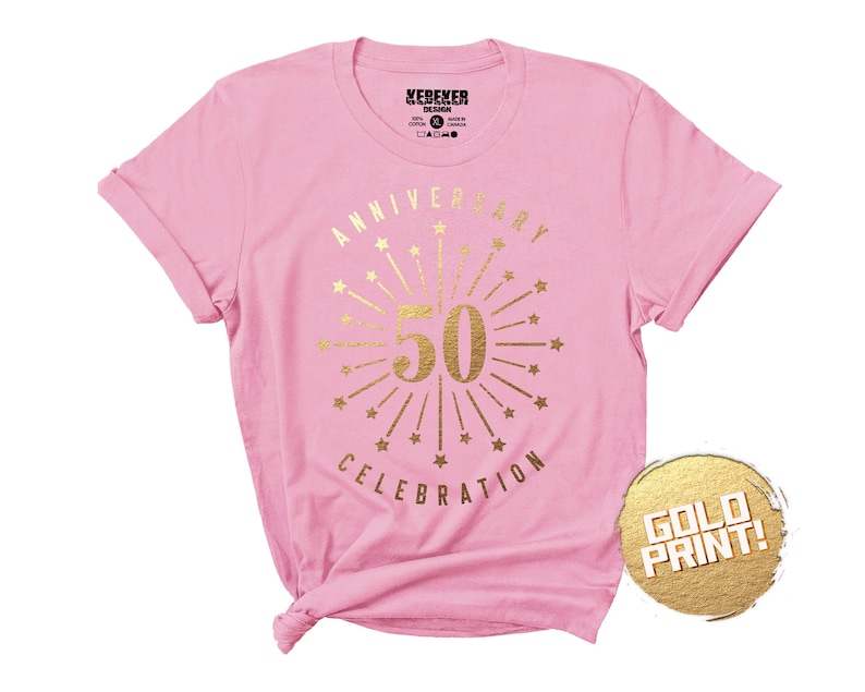 May include: Pink t-shirt with gold foil print that says "Anniversary Celebration" with a firework design and the number 50 in the center.