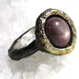 May include: A silver ring with a textured band and a large, oval-shaped, pink gemstone set in a gold bezel.