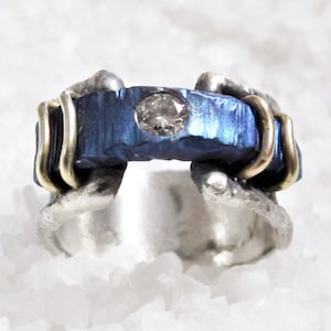 May include: A blue and silver ring with a clear stone set in the center. The ring is made of metal and has a unique design.