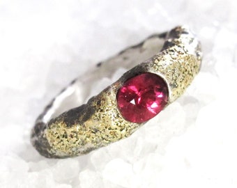 May include: A silver ring with a textured gold band and a red gemstone.