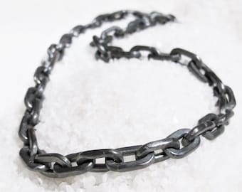 Può includere: Una collana a catena d'argento realizzata in metallo spesso e collegato. La catena è disposta su una superficie bianca.