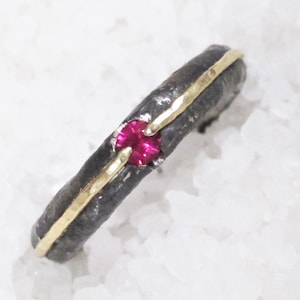 Puede incluir: Un anillo de plata con una banda delgada de oro y una pequeña piedra roja.