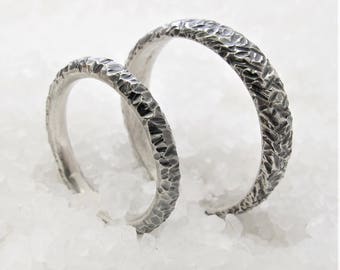 May include: Two silver wedding bands with a textured hammered finish. The bands are stacked on top of each other.
