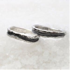 Op de afbeelding: Twee zilveren ringen met een zwart geoxideerde band. De ringen zijn getextureerd en hebben een gehamerde afwerking.