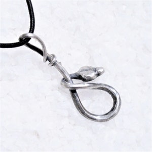 K&ouml;nnte beinhalten: Eine silberne Schlangen-Anh&auml;nger-Kette mit einem schwarzen Band. Die Schlange ist zu einer Schleife zusammengerollt, mit dem Kopf nach oben.