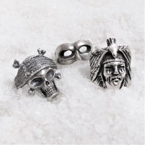 May include: Three silver-toned rings, one with a skull design, one with a Native American headdress design, and one with a mask design.
