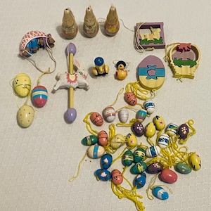May include: A collection of Easter-themed decorations, including painted wooden eggs, figurines, and a carousel toy. The eggs are in various colors and patterns, with yellow string attached. Other items include a wooden egg-shaped ornament and a basket.