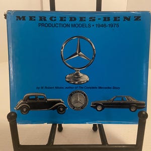 May include: A blue book cover with the title "MERCEDES-BENZ PRODUCTION MODELS 1946-1975". It features a silver Mercedes-Benz logo and illustrations of two black cars. The author's name is also visible.