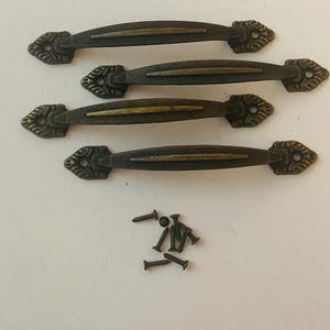 May include: Four arch-shaped metal drawer pulls with an antique bronze finish, featuring decorative leaf-like ends and a central raised ridge. The set includes eight small metal screws for installation, arranged in a cluster below the handles.