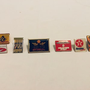 May include: A collection of vintage Shell and Havoline racing pins. The pins feature various designs, including the Shell logo, gas pumps, and the Havoline star. Some pins have text like "Grand Prix" and "Volunteer Staff."