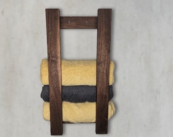 May include: A dark brown wooden towel rack with three towels stacked on it. The towels are yellow and gray.