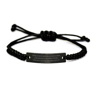 Pode incluir: Pulseira trançada preta com uma etiqueta de metal preto que diz "Portanto, meus amados irmãos, sede firmes, inabaláveis, abundando sempre na obra do Senhor, sabendo que o vosso trabalho no Senhor não é em vão."