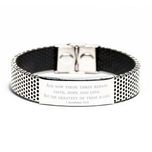 May include: A black and silver bracelet with a metal plate engraved with the quote "AND NOW THESE THREE REMAIN: FAITH, HOPE AND LOVE. BUT THE GREATEST OF THESE IS LOVE. 1 Corinthians 13:13."
